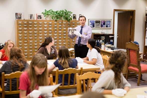 Professor Wenxian Zhang holding and pointing to a book while lecturing a class of seated students