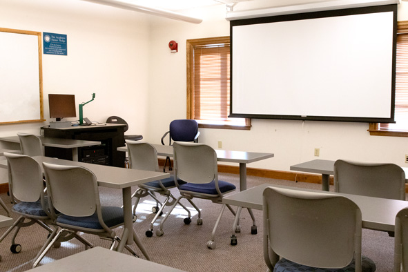 gray tables with gray chairs tucked underneath facing a wall with a projector screen framed by two windows on each side