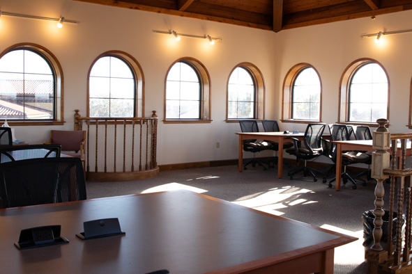 a room filled with brown tables and black rolling chairs at each table, with arched windows along the walls, overlooking the Rollins campus